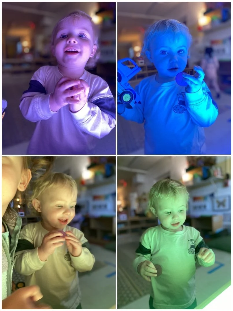 Four images of a young child in a room with colorful lights, each image showing the child illuminated by different colored lights: purple, blue, yellow, and green. The child is wearing a light-colored shirt with dark sleeves in the first, third, and fourth images, and has a toy car or object in the second image.