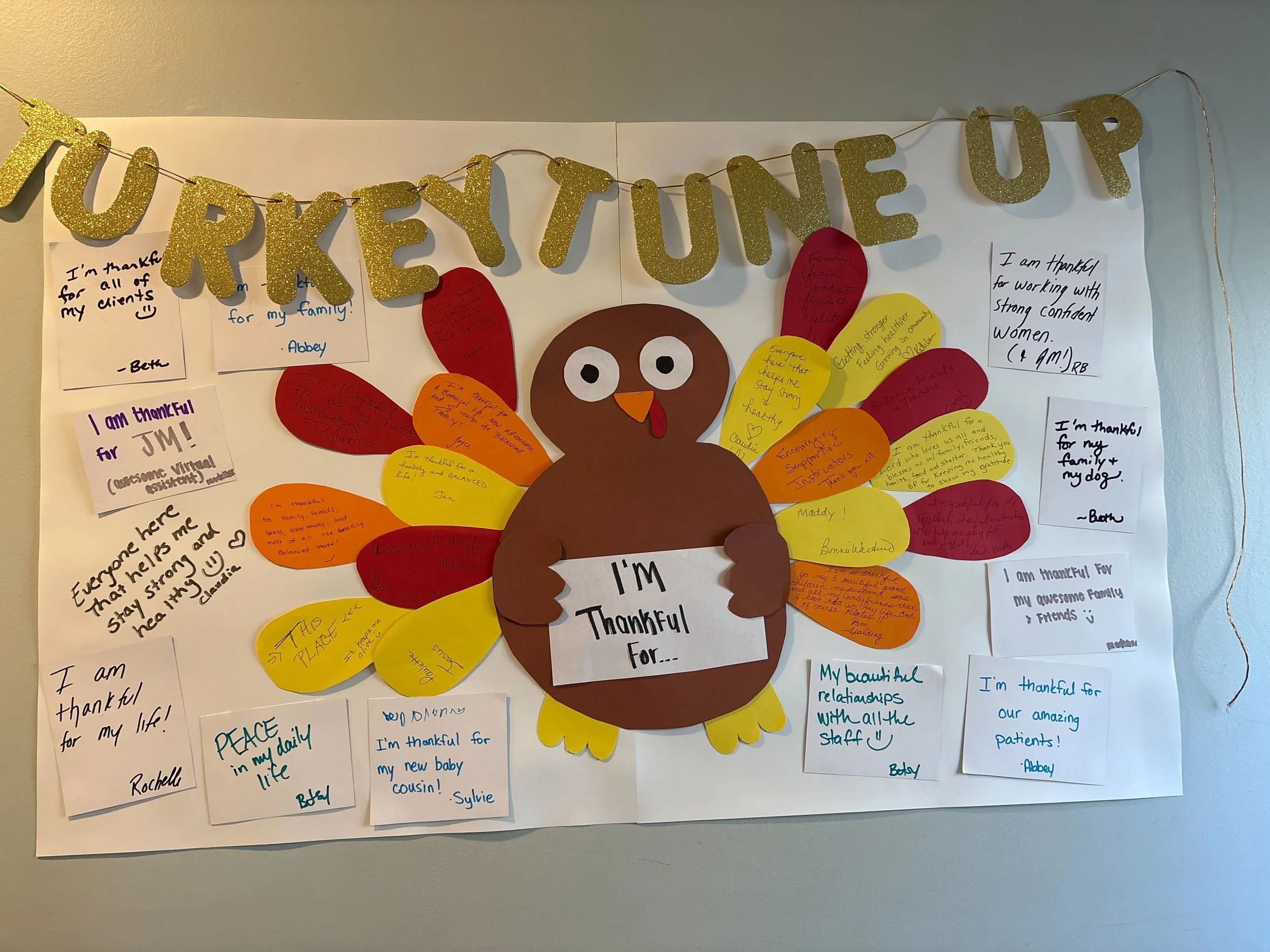 A colorful gratitude bulletin board featuring a large paper turkey with the words "I'm thankful for..." and handwritten notes on colored paper turkeys and white sheets, expressing gratitude for various people, experiences, and aspects of life.