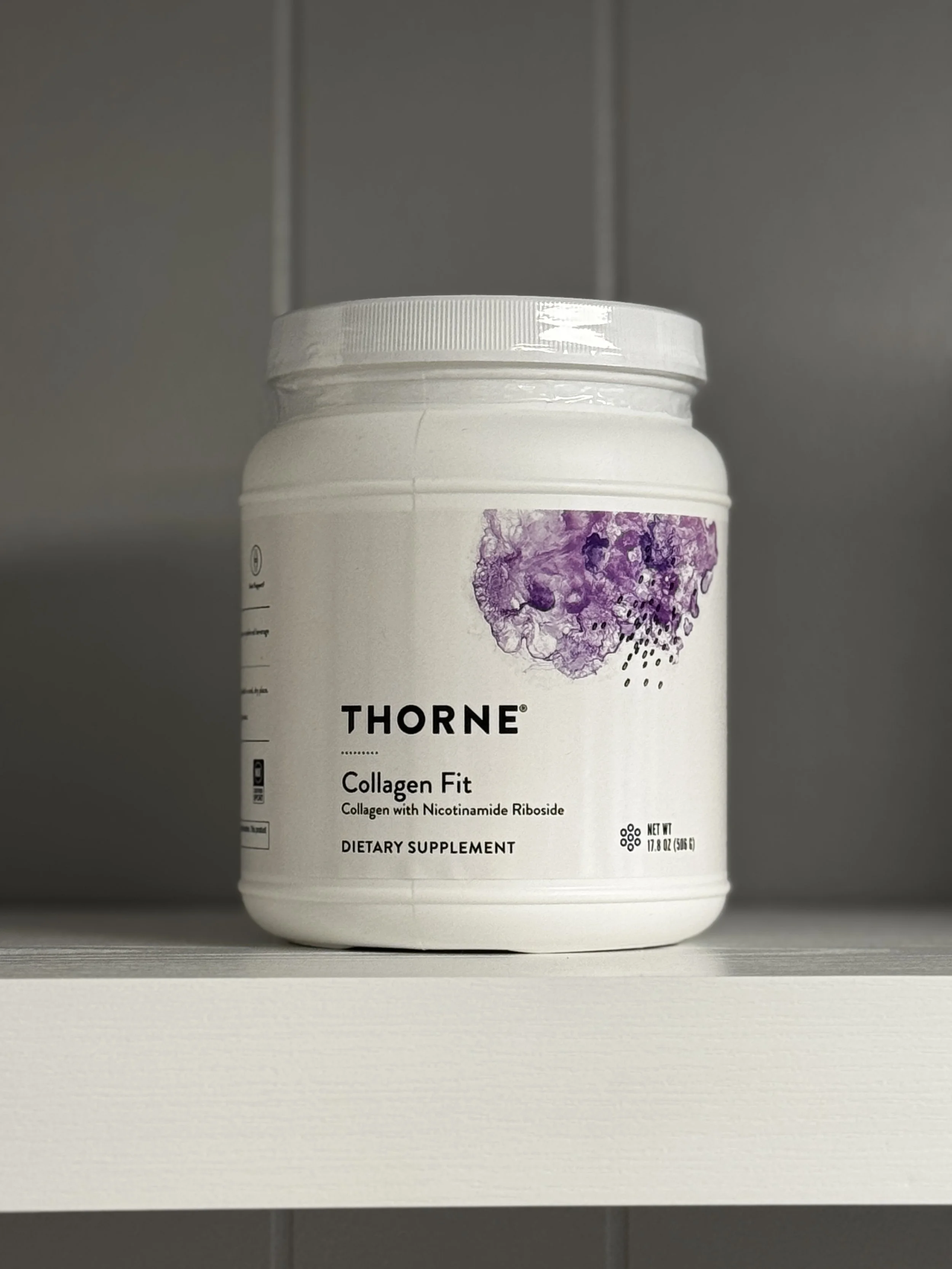 A white container of Thorne Collagen Fit dietary supplement on a white shelf against a grey wall.