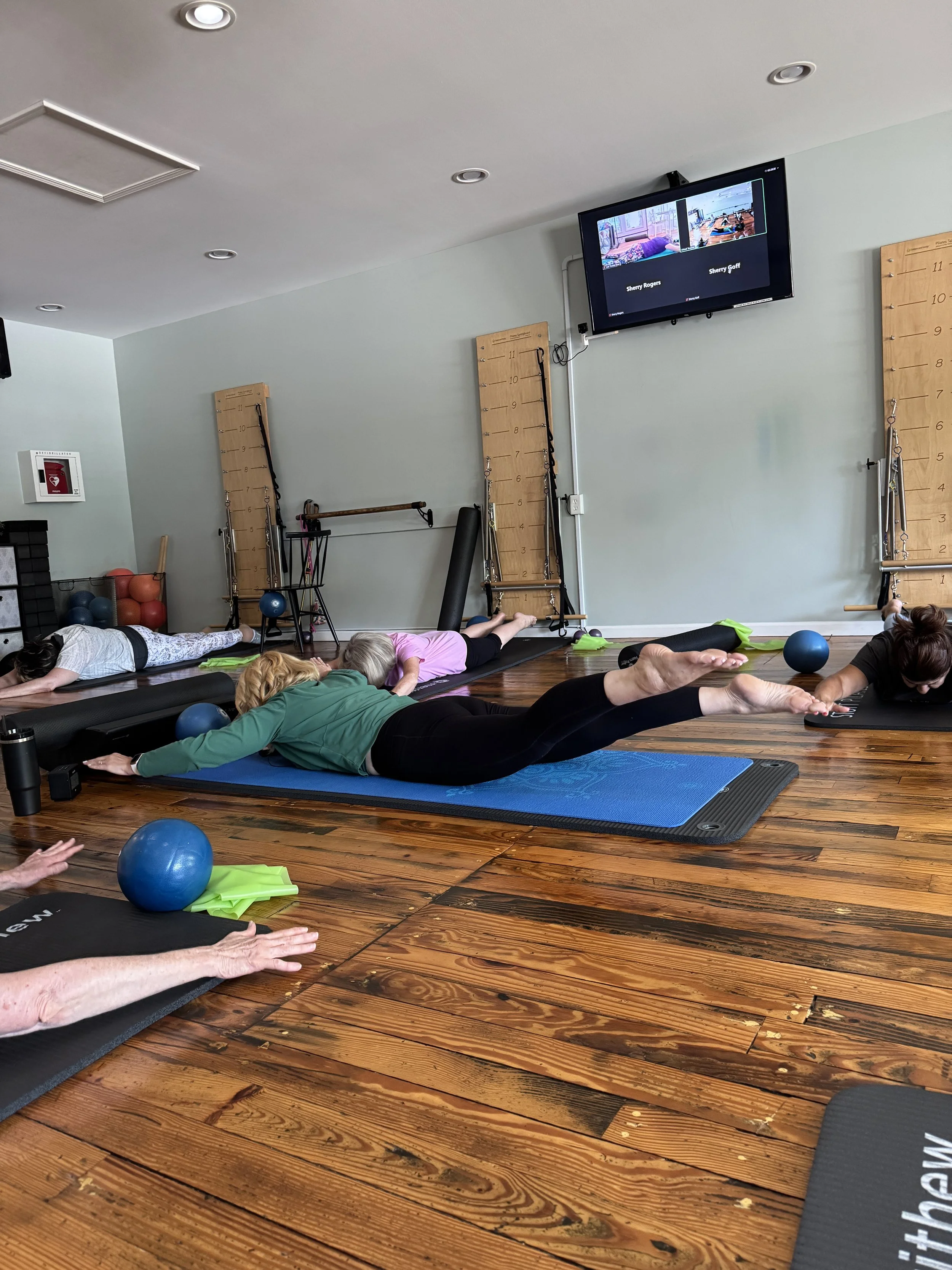 Participants lying on mats and practicing STOTT Pilates in Midland, Michigan, with exercise balls and equipment visible around the room.