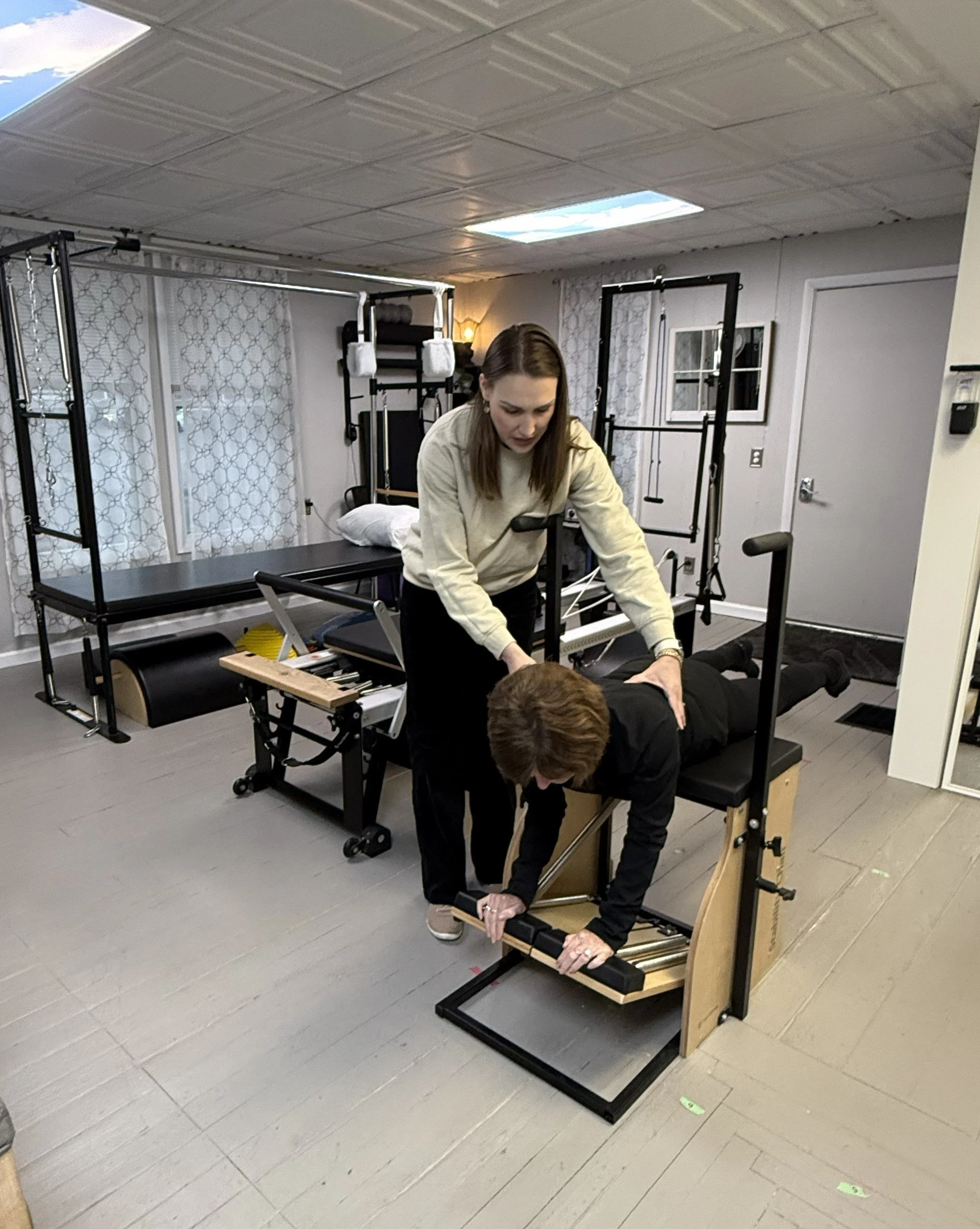 A woman is lying face down on a treatment table while another woman, standing beside her, performs physical therapy in a cozy and private gym.