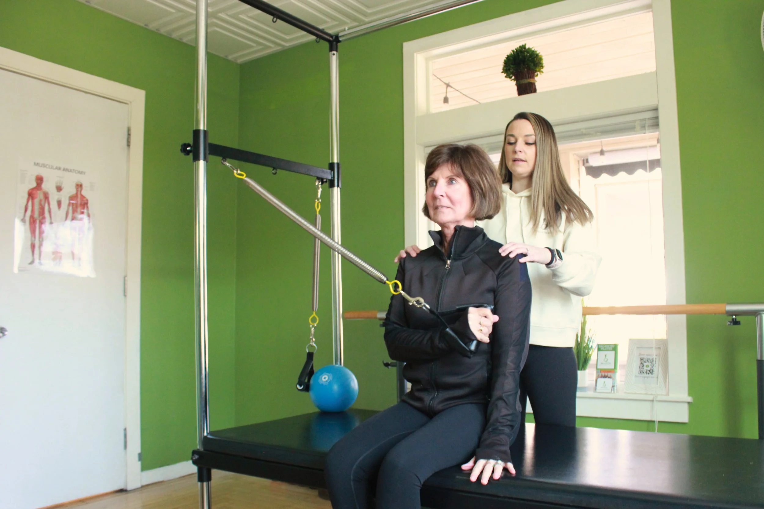 A woman sits on a black platform with her hands supporting her as she performs an exercise in a private Pilates session at Balanced Pilates and Wellness Boutique in Midland, Michigan.