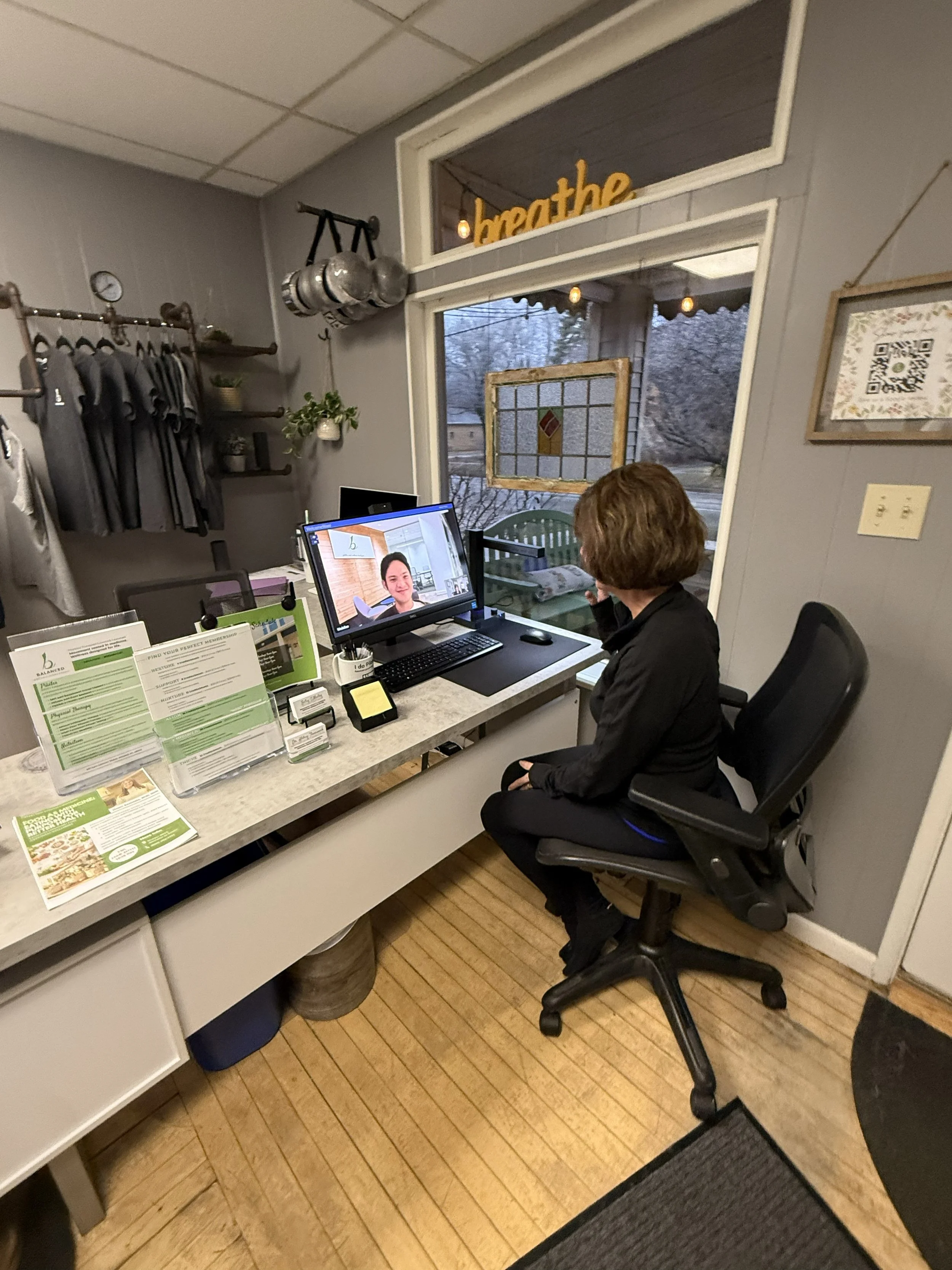 A woman sitting at a reception desk in an office, engaged in a video call on with Balanced virtual assistant for physical therapy scheduling in Midland, Michigan.