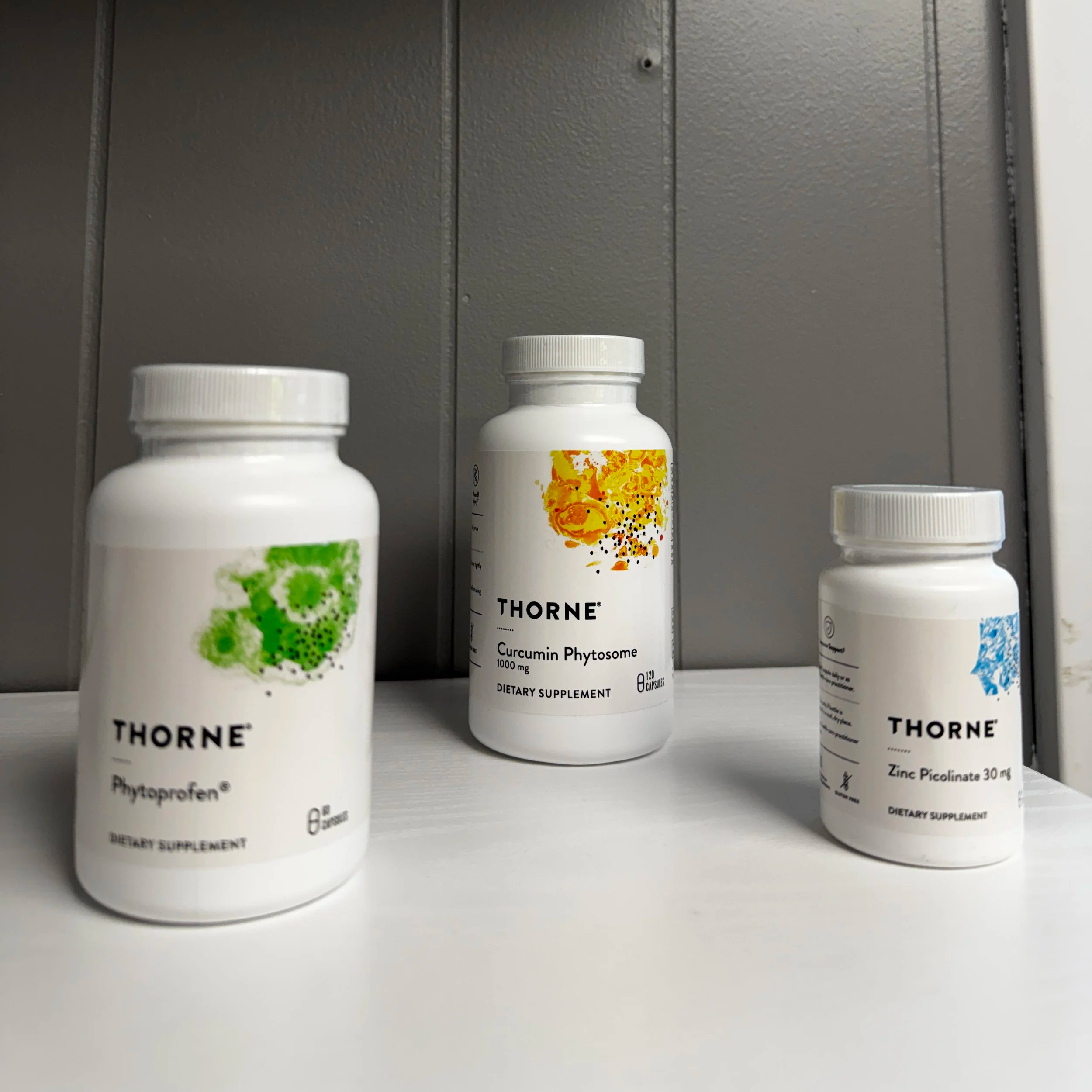 Three white supplement bottles on a store shelf, with labels indicating they are dietary supplements, including one labeled 'Thorne Curcumin Phytosome 1000 mg'.
