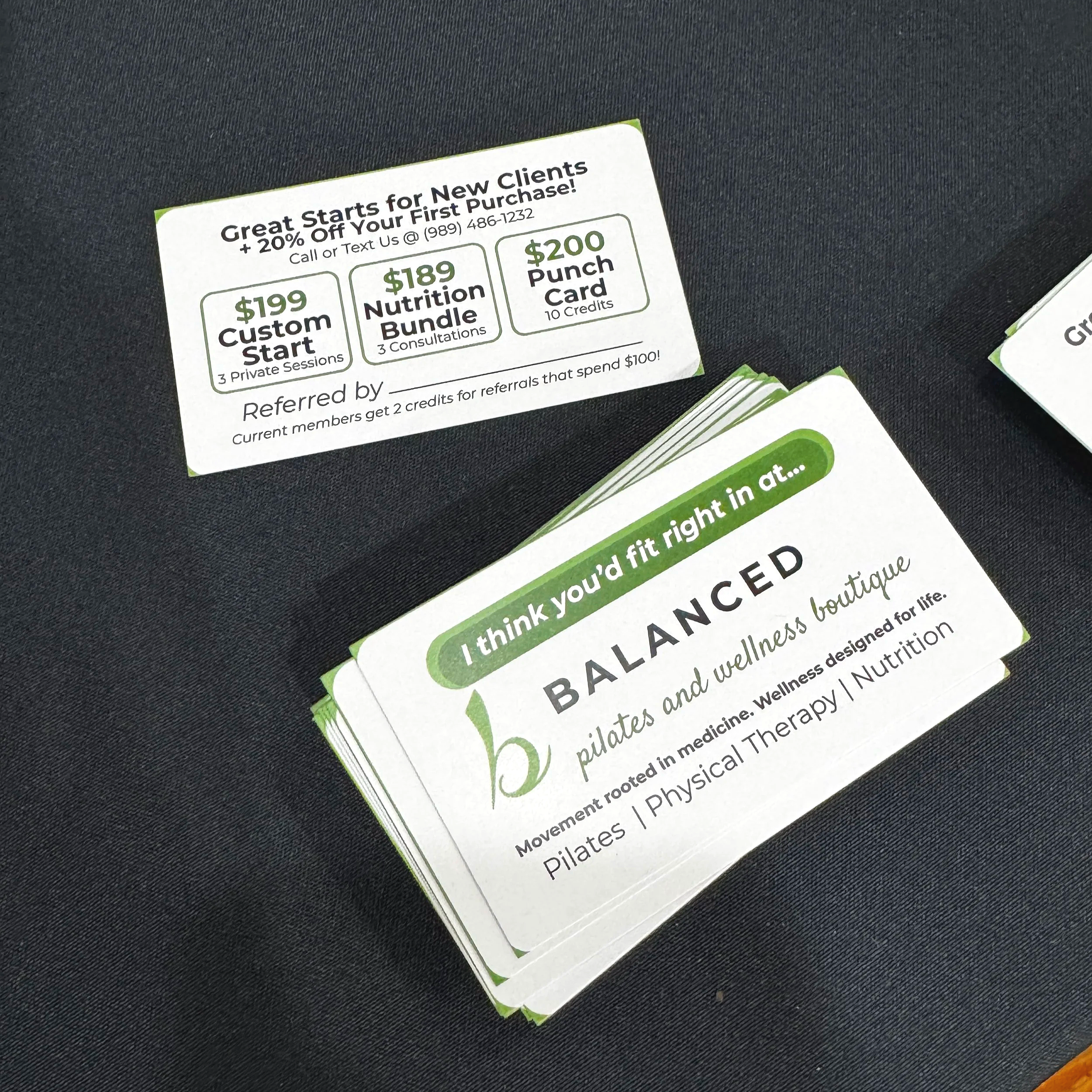 A stack of business cards for the referral program. The card promotes special offers for new clients, including a $199 custom start package, an $189 nutrition bundle, and a $200 punch card. The cards have green and black text on a white background.