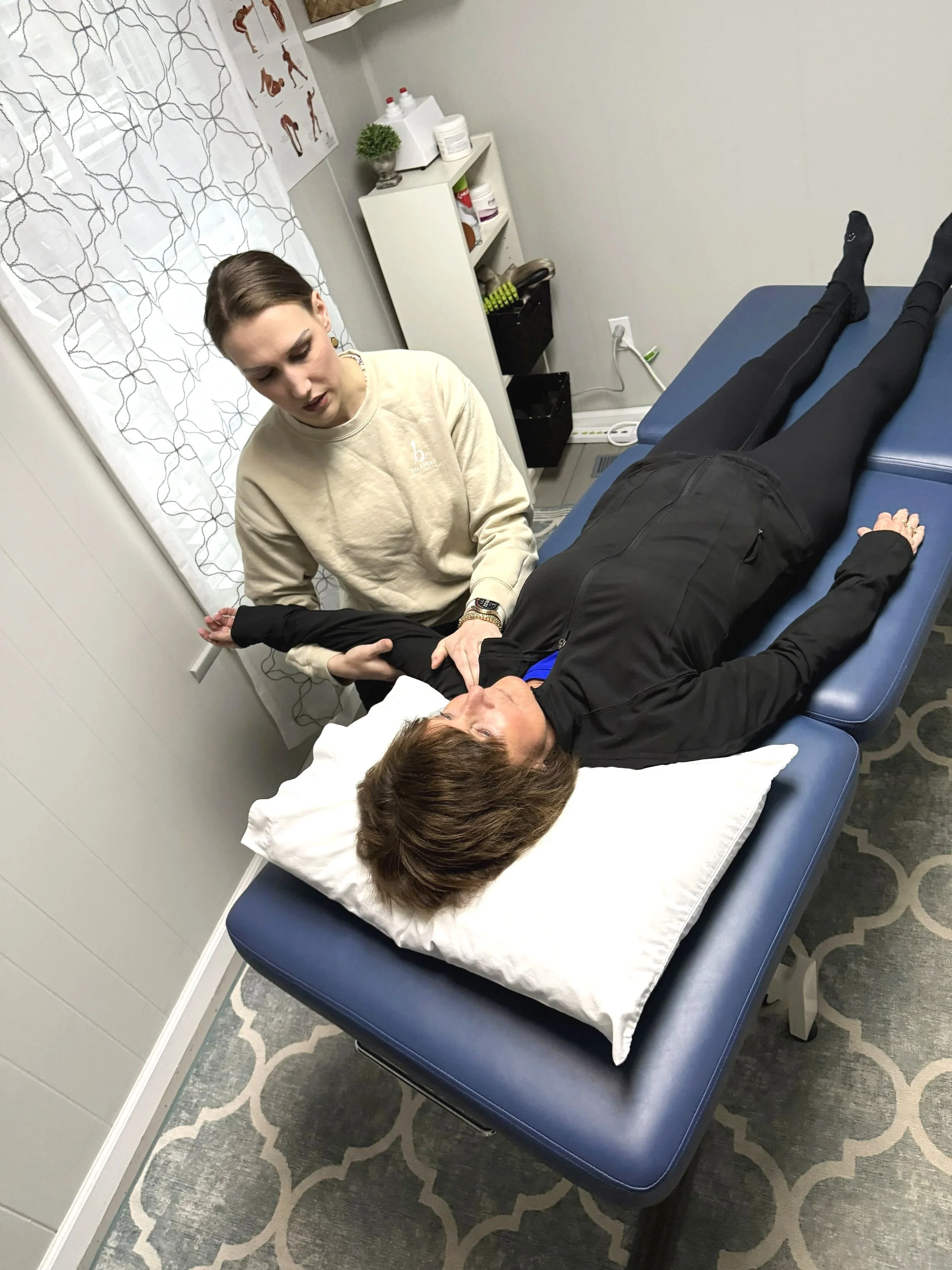 A woman lying on her back on a blue examination table for physical therapy at Balanced Pilates and Wellness Boutique in Midland, Michigan.