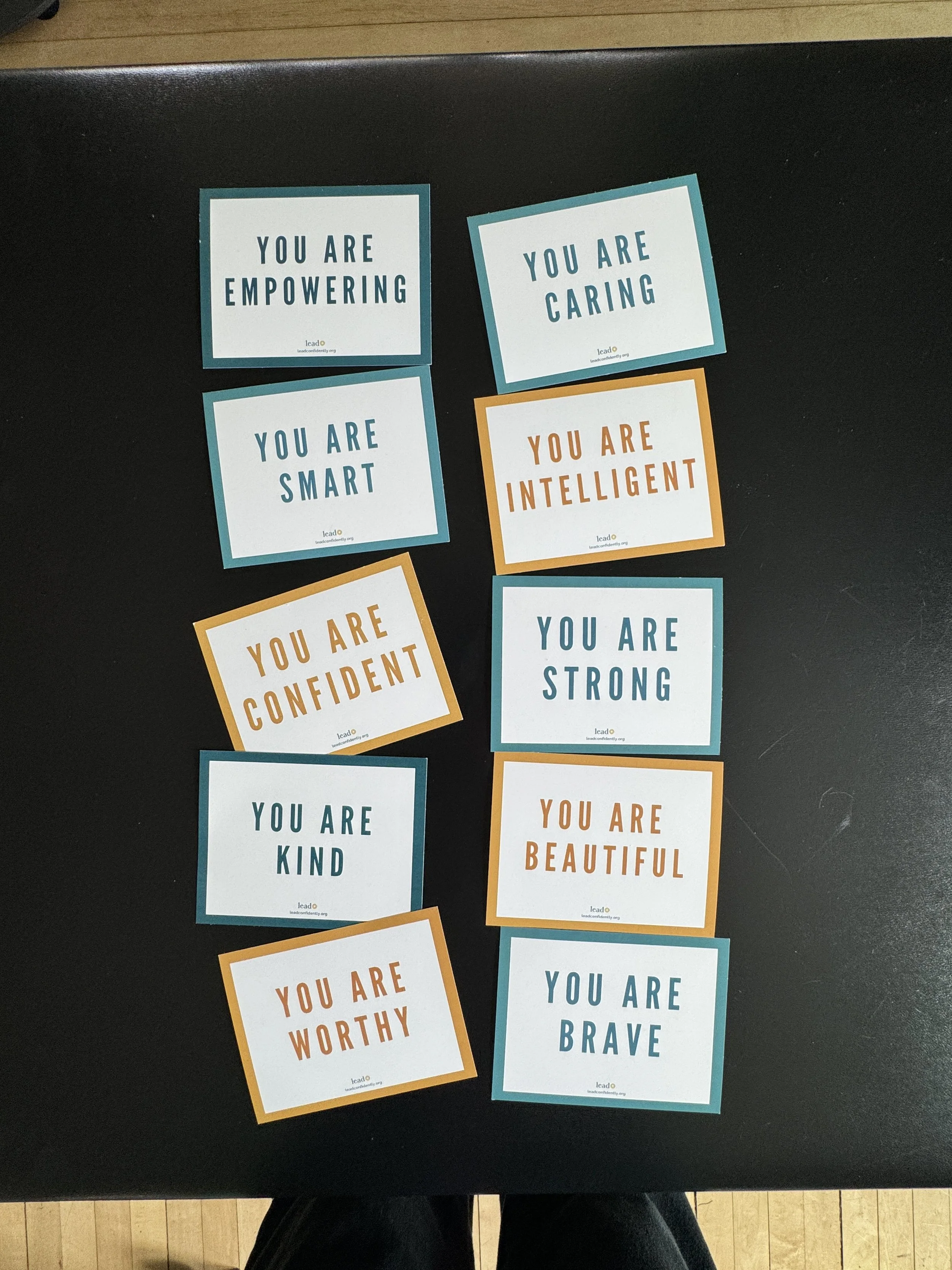 A collection of motivational and positive affirmation cards on a black surface. The cards display messages such as 'You are empowering,' 'You are caring,' 'You are smart,' 'You are intelligent,' 'You are kind,' 'You are confident,' 'You are worthy,' 