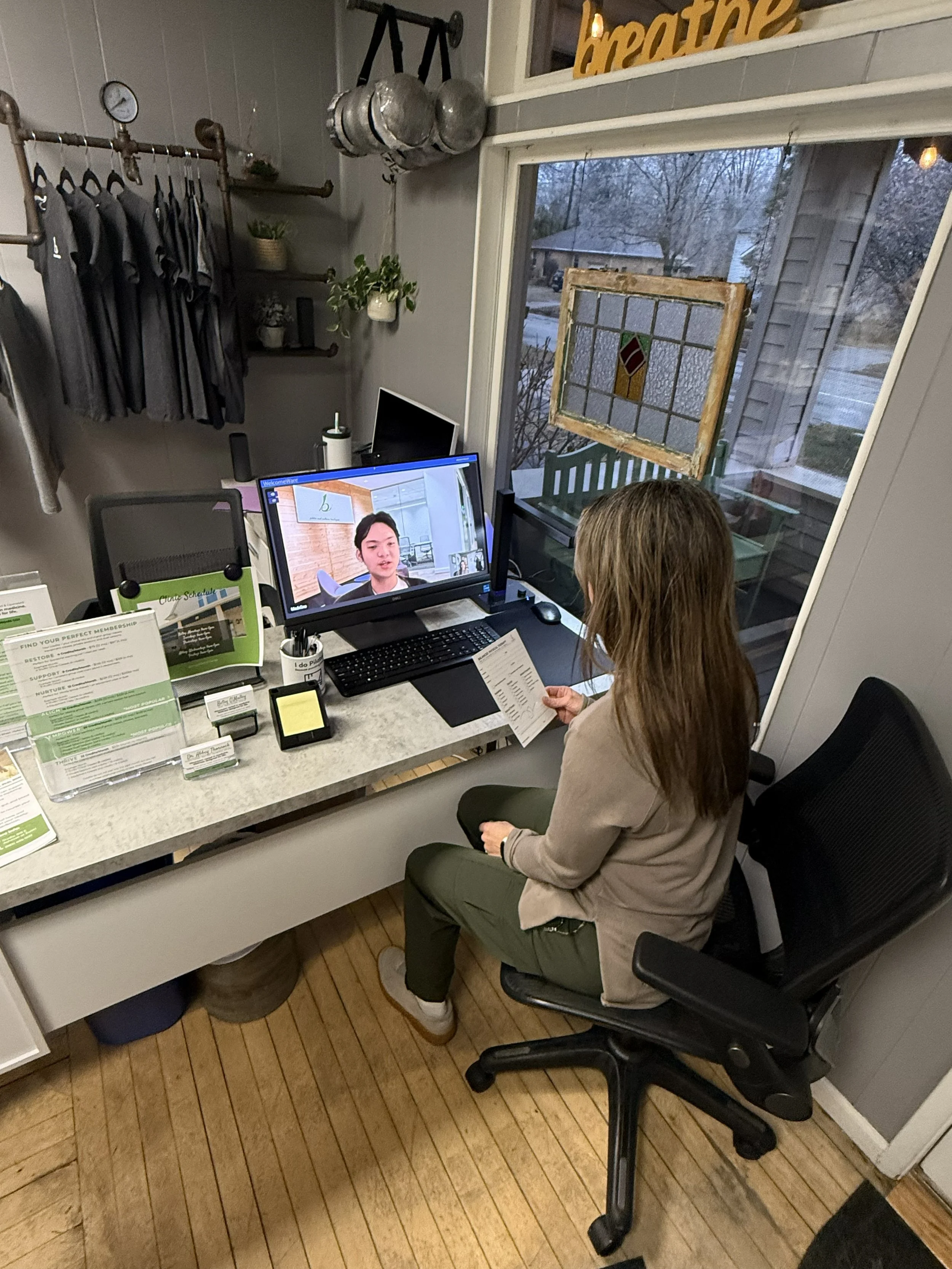 A woman sitting at a desk in a cozy office, talking with Balanced Pilates virtual assistant for scheduling appointments.