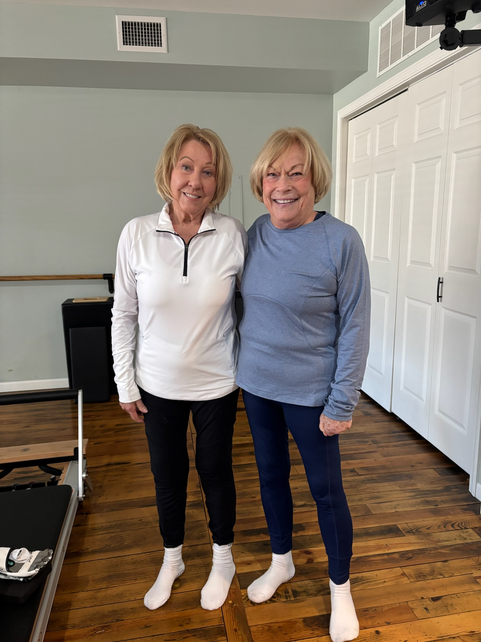 Two women standing indoors, wearing socks and standing in Balanced Pilates and Wellness Boutique in Midland, Michigan.