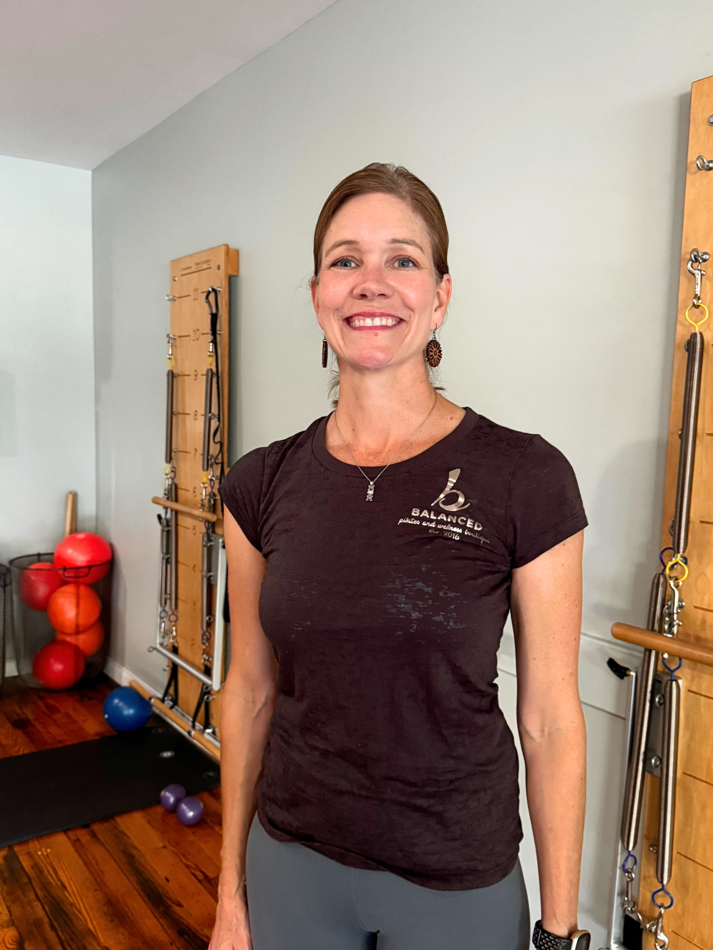 Pilates instructor Heather Zahn smiling and looking at the camera in a fitness studio with exercise equipment in the background.