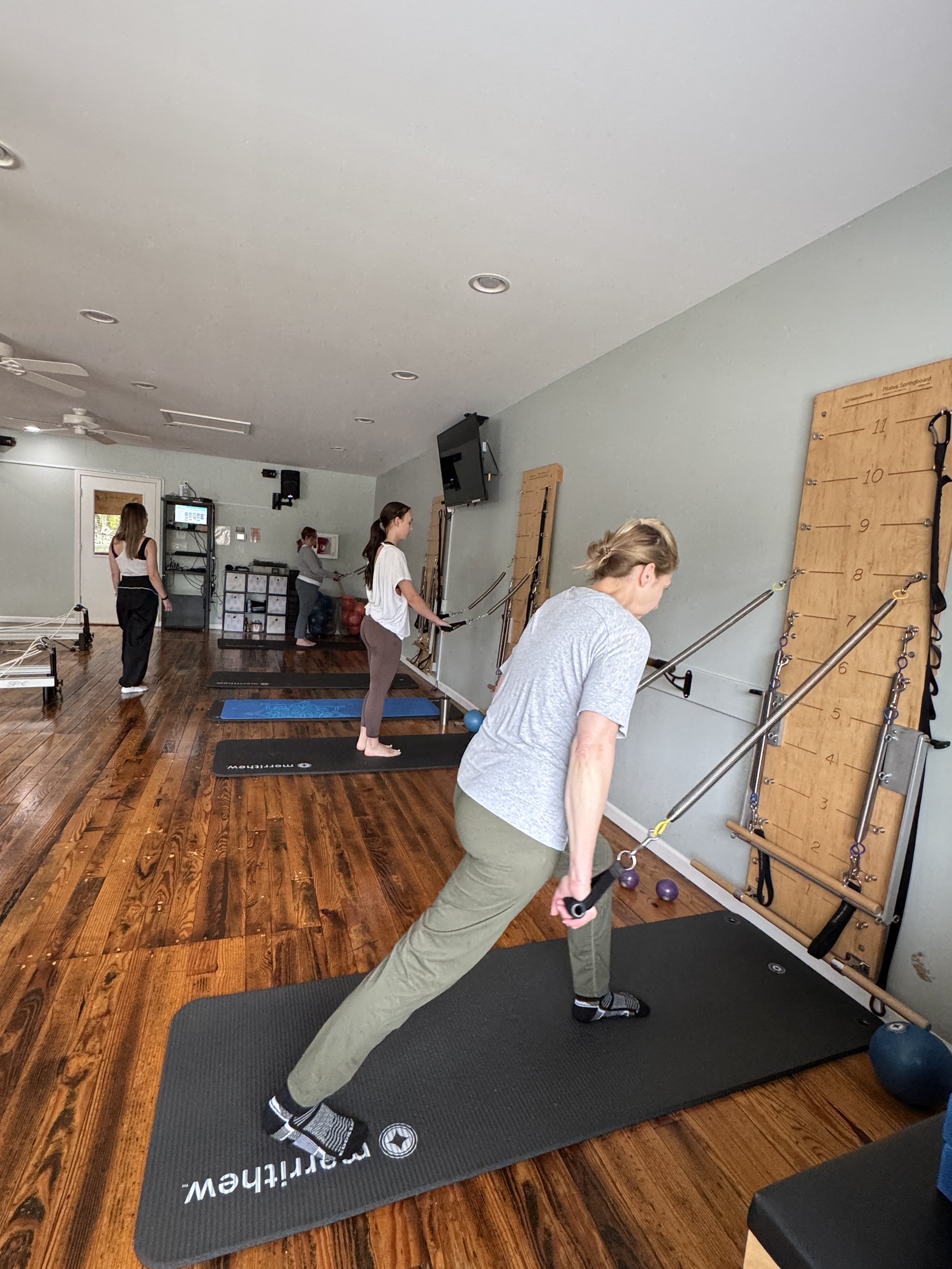Women participating in a Pilates Springwall class performing resistance band exercises on mats and a wall-mounted board with resistance bands.