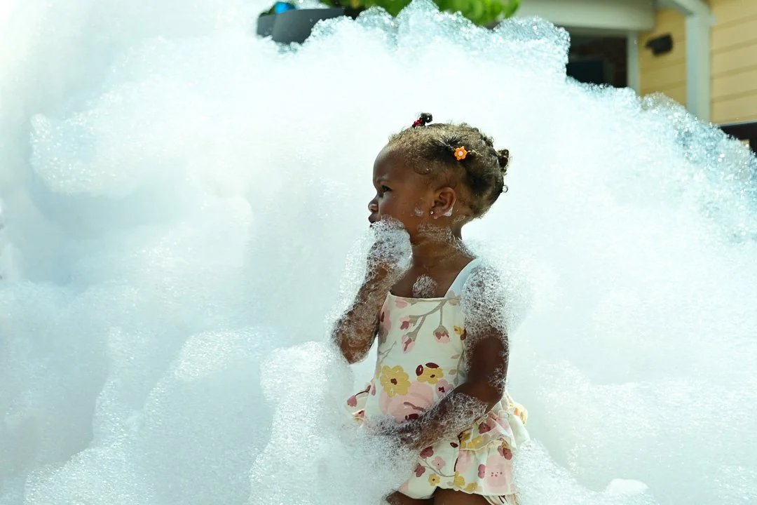 Young girl in a colorful floral dress playing in a foam-filled bubble bath.