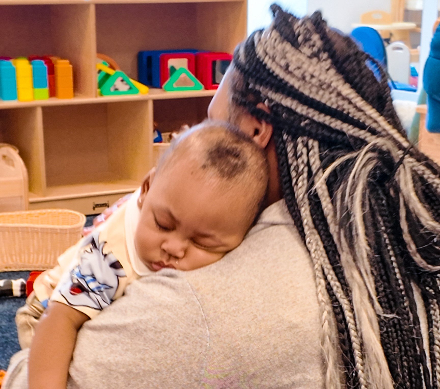 A young child sleeping on an adult's shoulder in a colorful indoor play area.