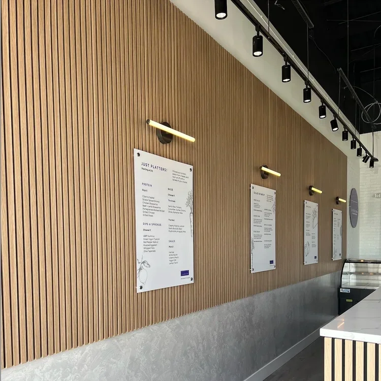 A modern restaurant menu display on a wooden slat wall with black track lighting and wall-mounted light fixtures.