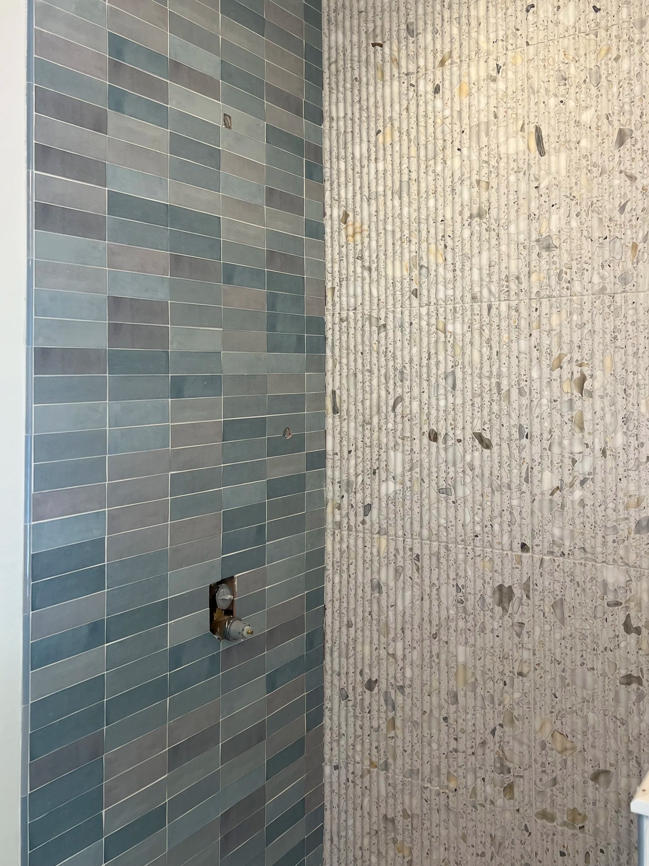 Bathroom with blue tiled wall, pipes, and plumbing fixtures, next to a white shower curtain with shell-like patterns.
