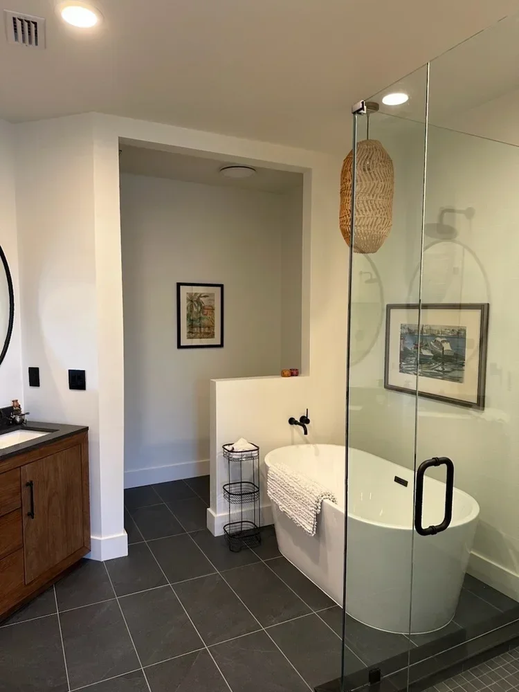 Modern bathroom with a standalone bathtub, glass shower enclosure, wooden vanity, wall art, and decorative woven light fixture.