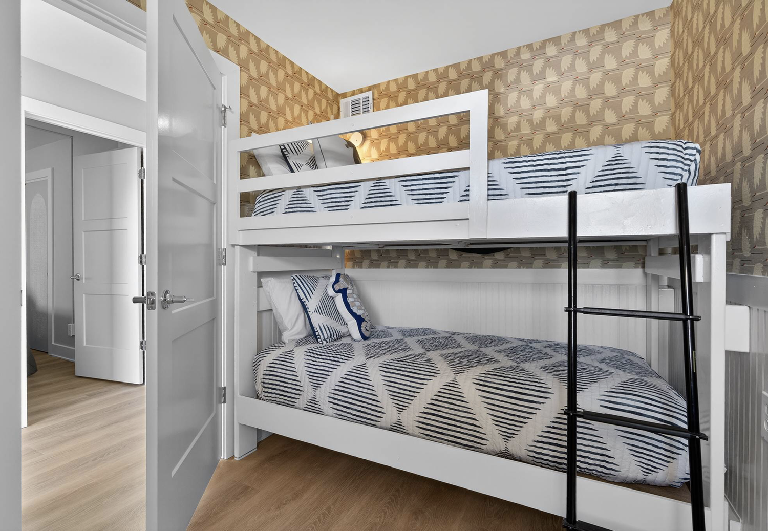 White bunk bed with a ladder in a room with patterned wallpaper and wooden flooring.