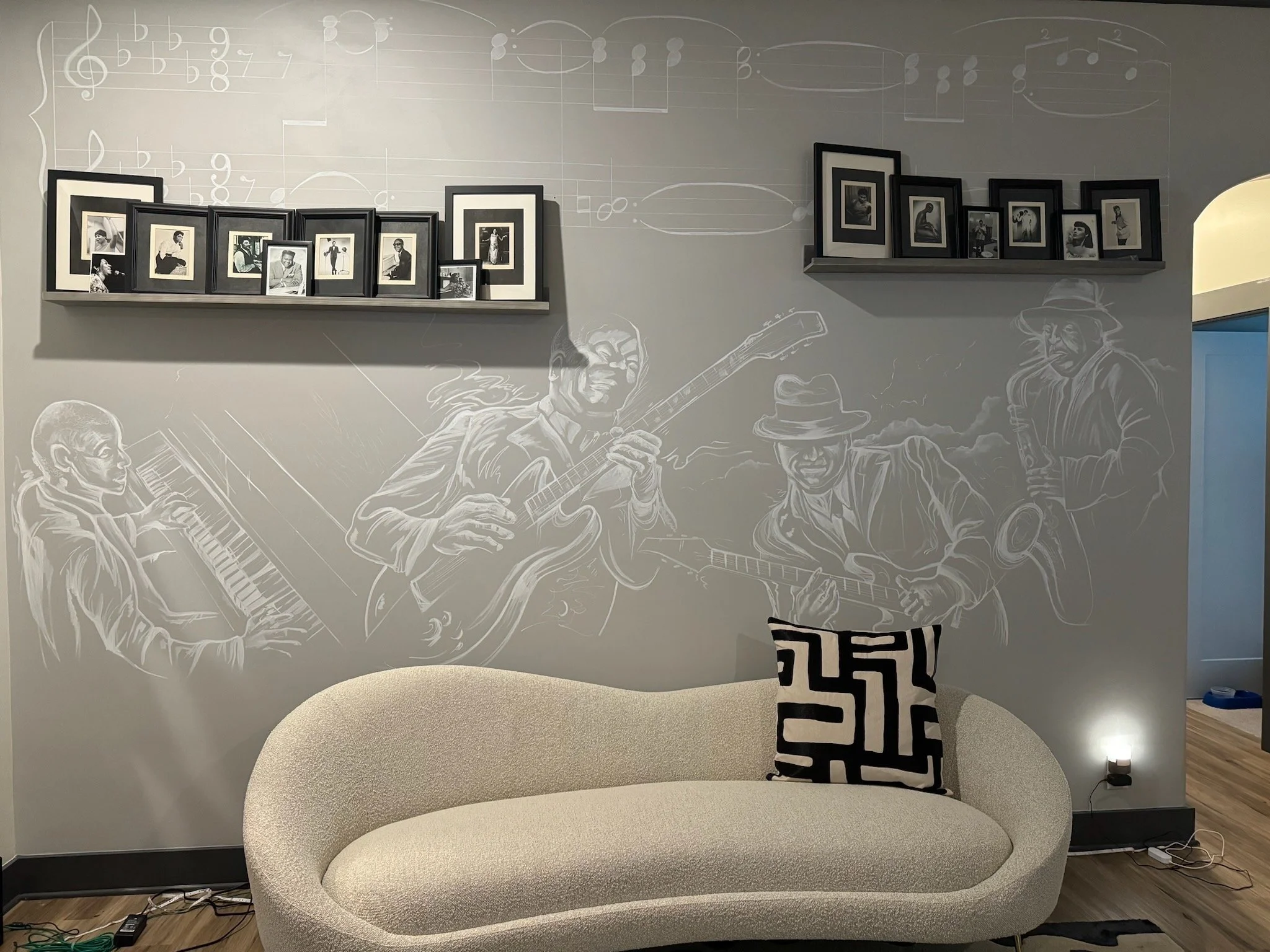 A wall with musical note ledgers and two shelves holding numerous framed black and white photographs. The photos showcase various people, some with musical instruments or posing, and are arranged in an overlapping manner. The wall also features an an