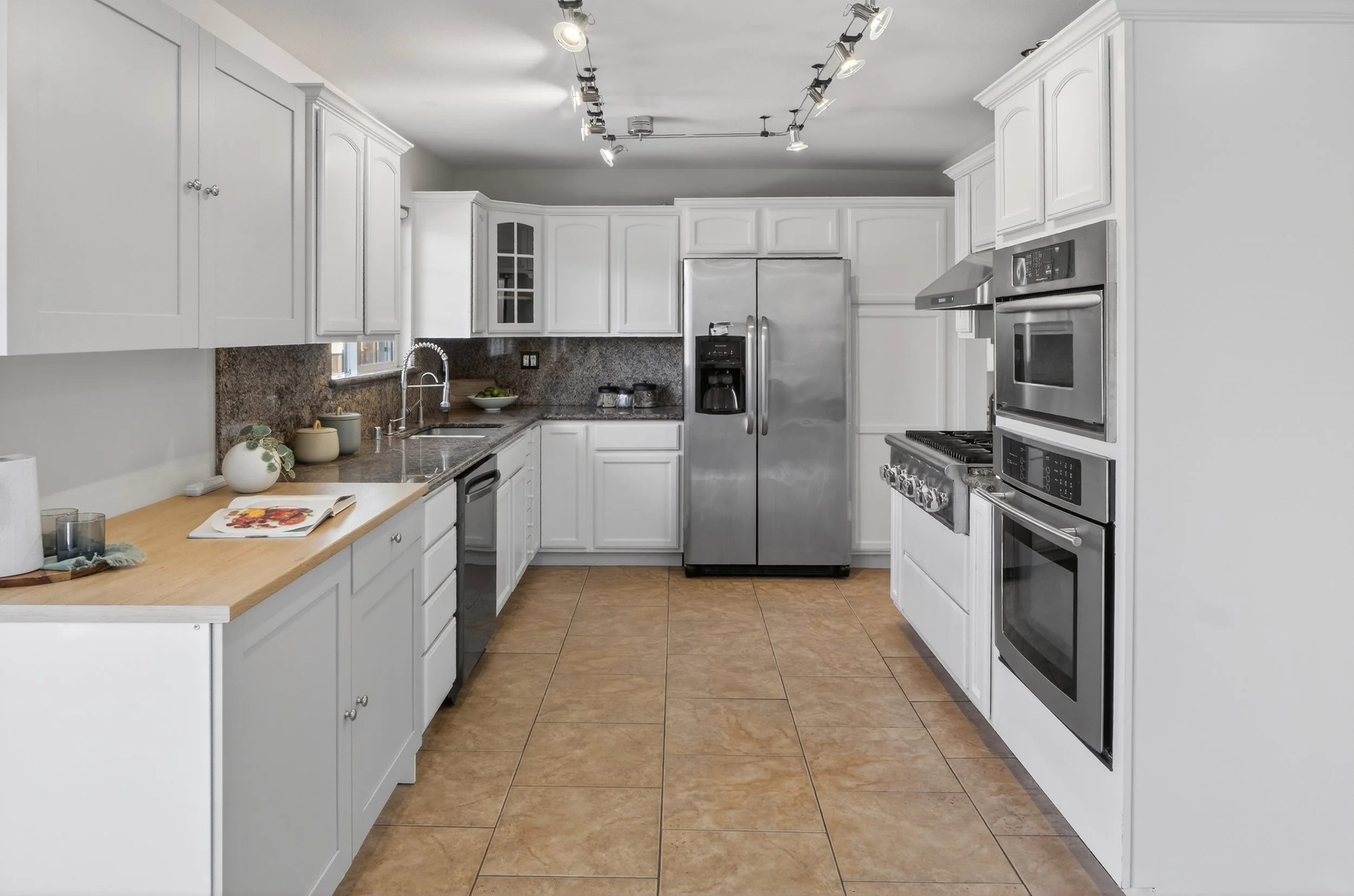 Pleasanton Kitchen with white cabinets, stainless steel refrigerator, stove, double oven, granite countertops, and tan tile flooring.