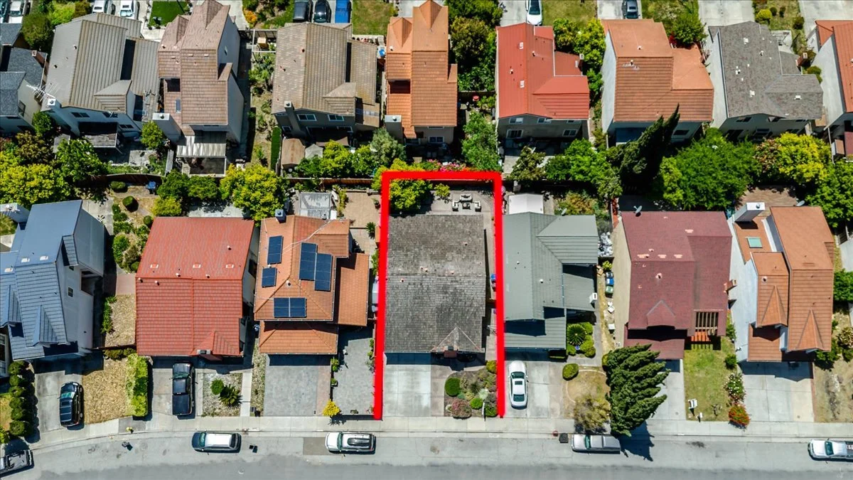 Aerial view of a residential neighborhood with houses, trees, and parked cars. A house is outlined in red in the center of the image.