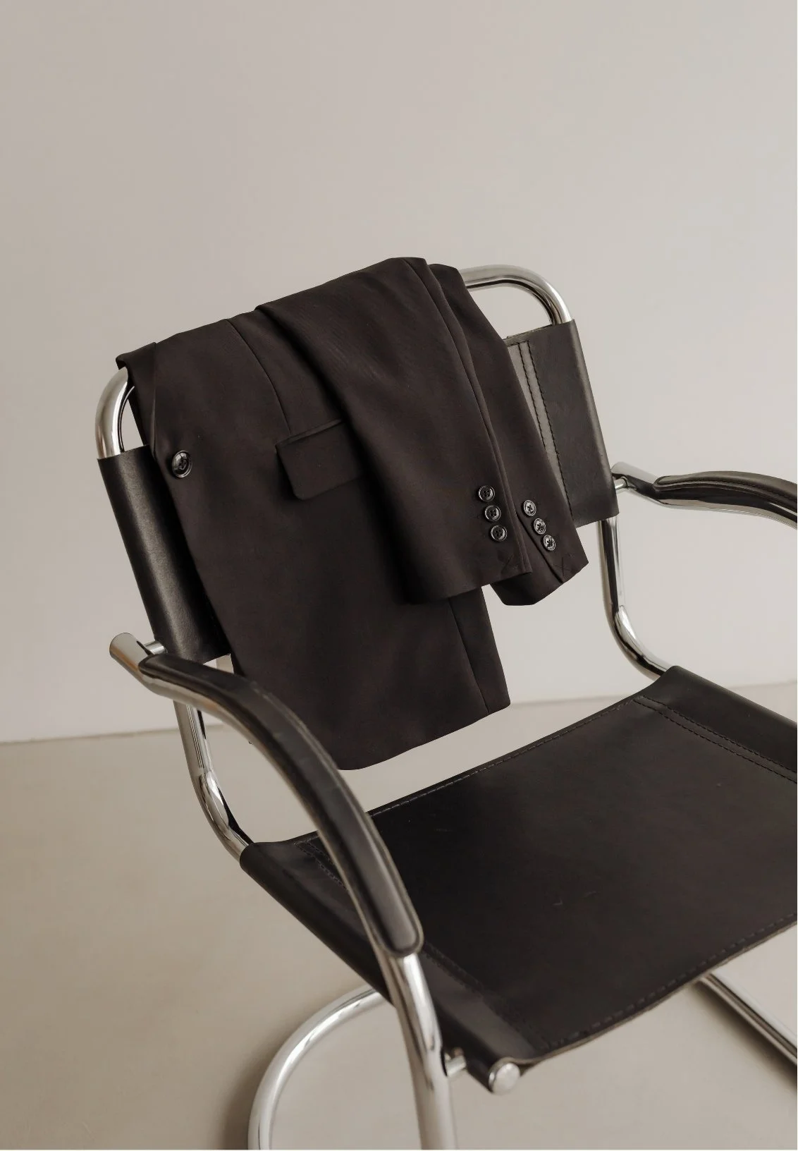 Black blazer and matching pocket square draped over the back of a modern black leather and chrome chair.