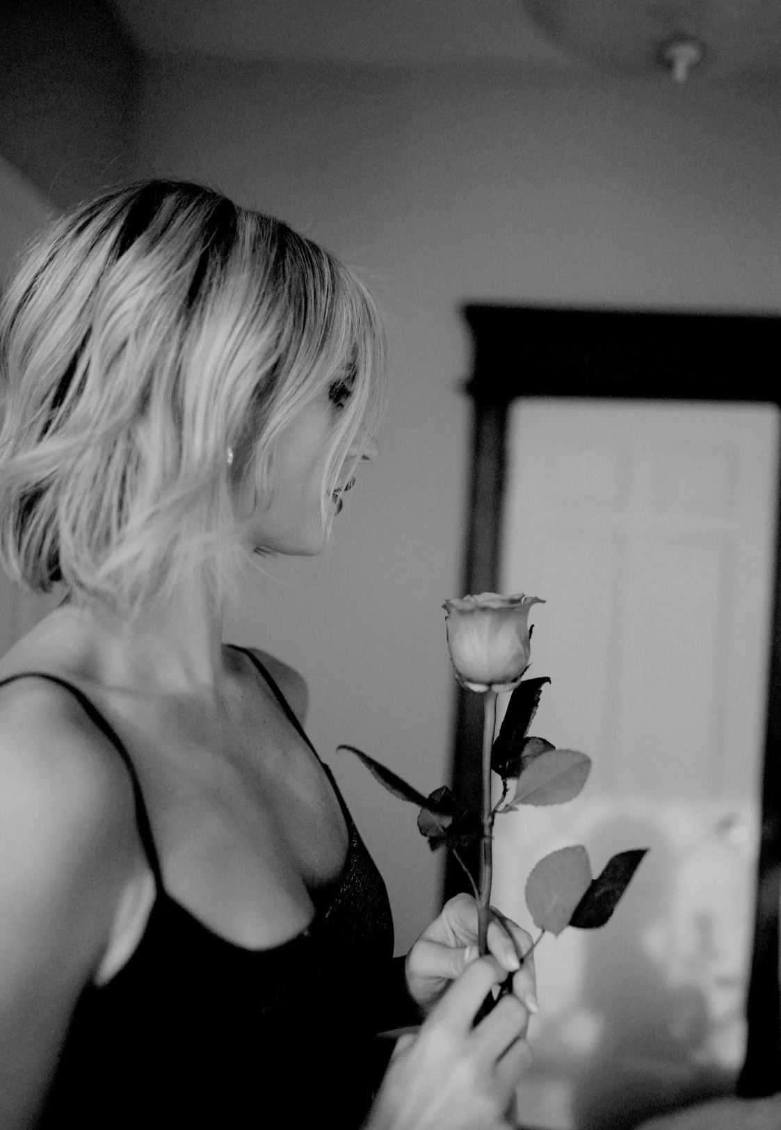 A woman with shoulder-length hair holding a rose, looking at it.