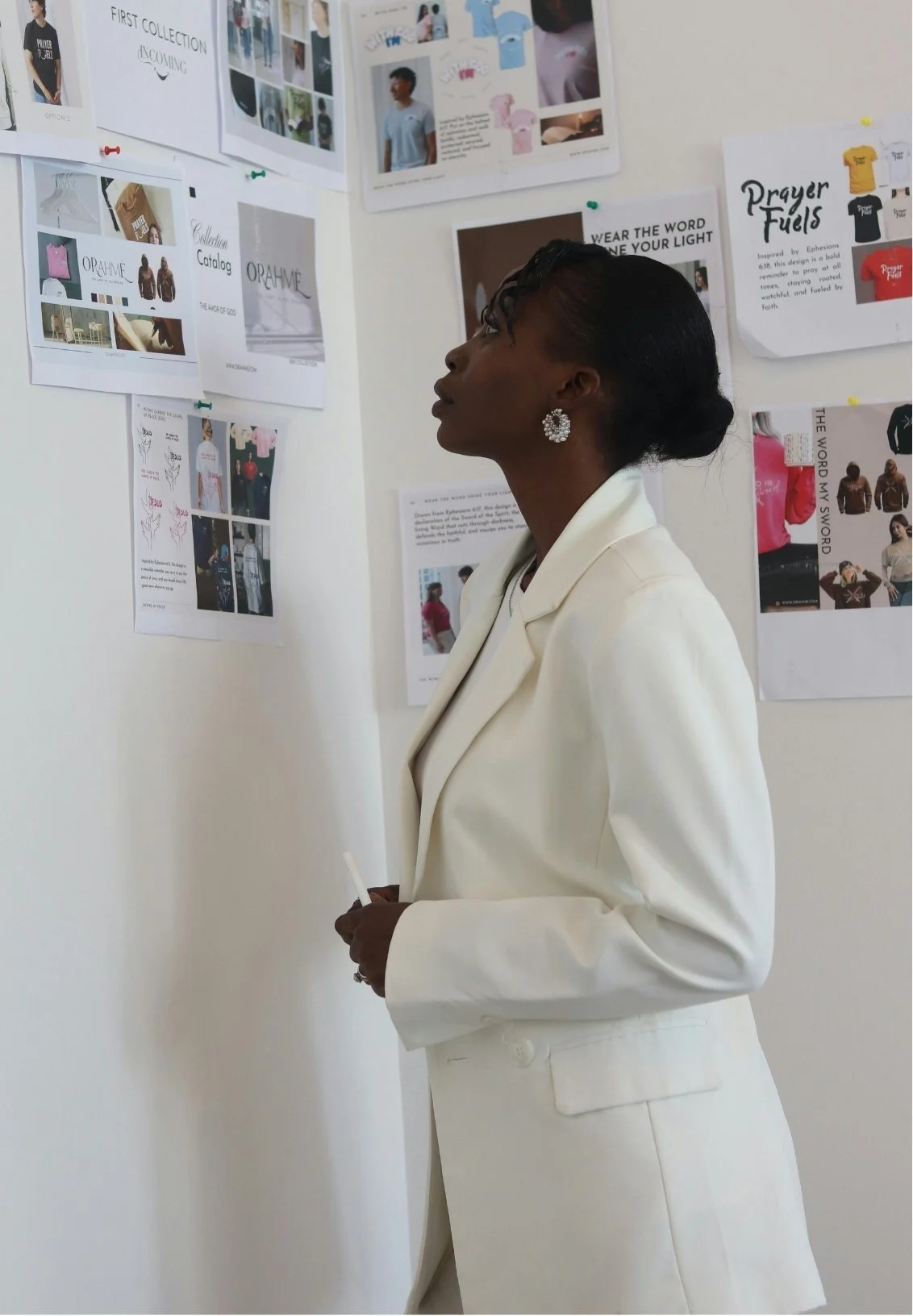 A woman in a white blazer looking at fashion or design concept boards on a white wall.