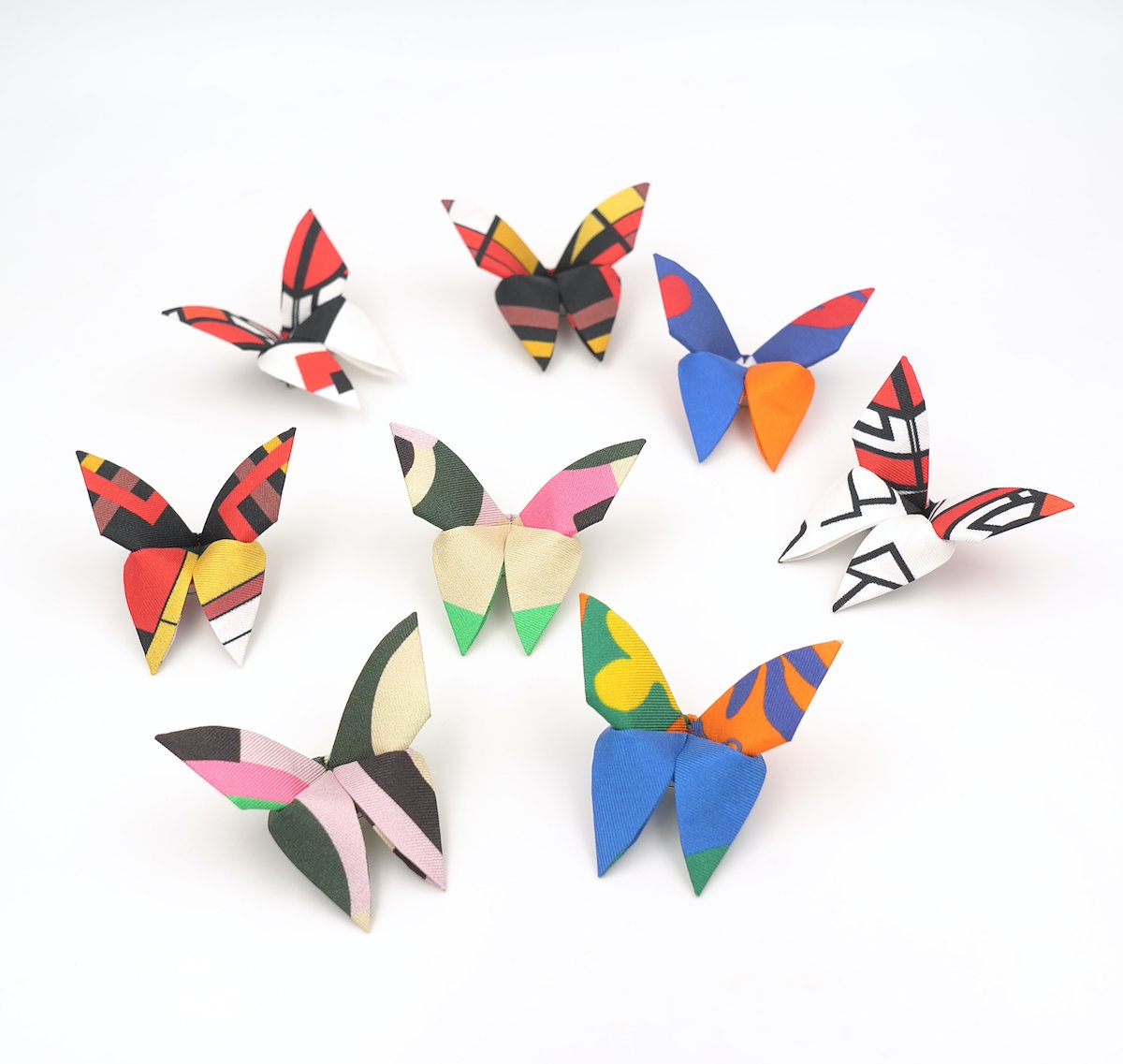 Huit papillons en papier colorés avec des motifs variés, disposés sur un fond blanc.