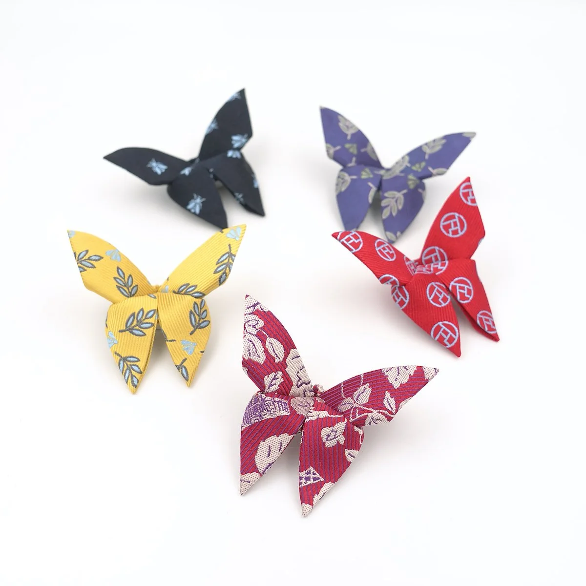 Cinq papillons en tissu coloré avec différents motifs, disposés sur un fond blanc.