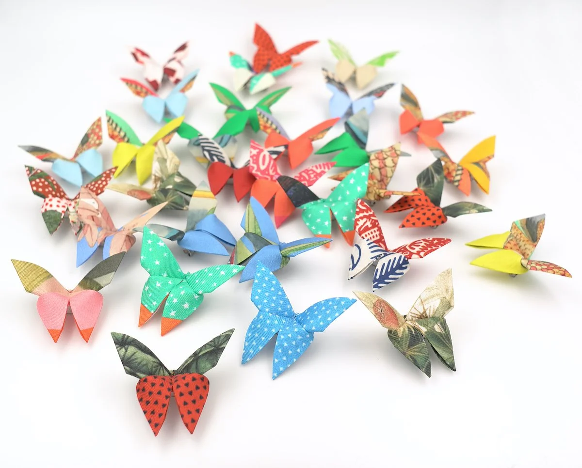 Plusieurs papillons en papier coloré disposés sur un fond blanc.