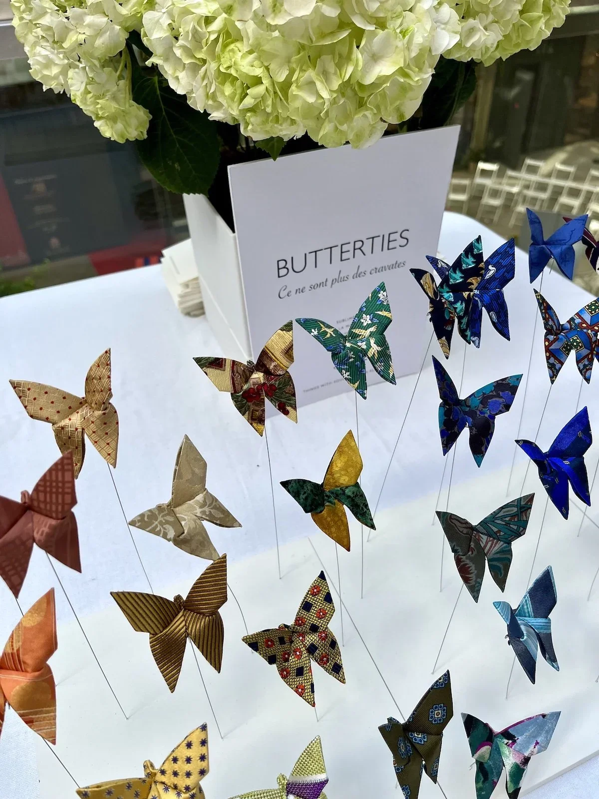Fleurs d'hortensia blanches et un panneau indiquant 'BUTTERLIES Ce ne sont plus des cravates' avec des papillons en papier colorés suspendus.