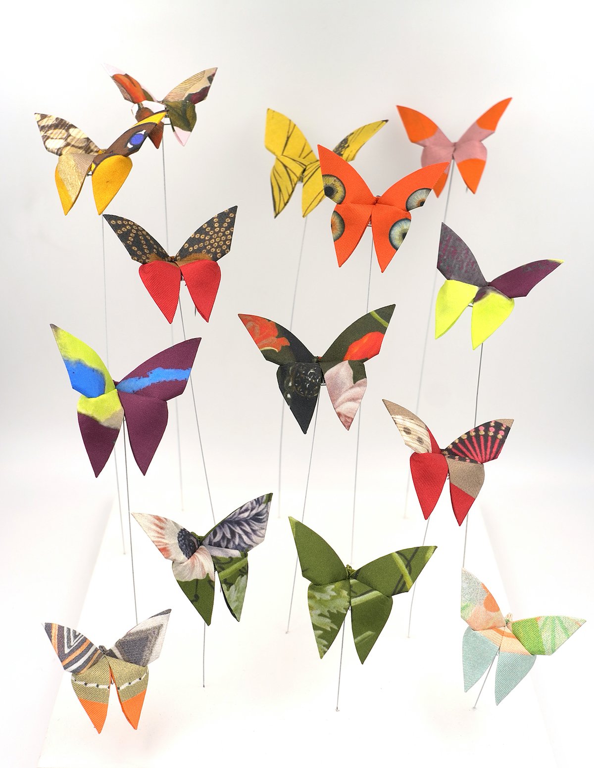 Collection de papillons en papier colorés suspendus par des fils fins contre un fond blanc.