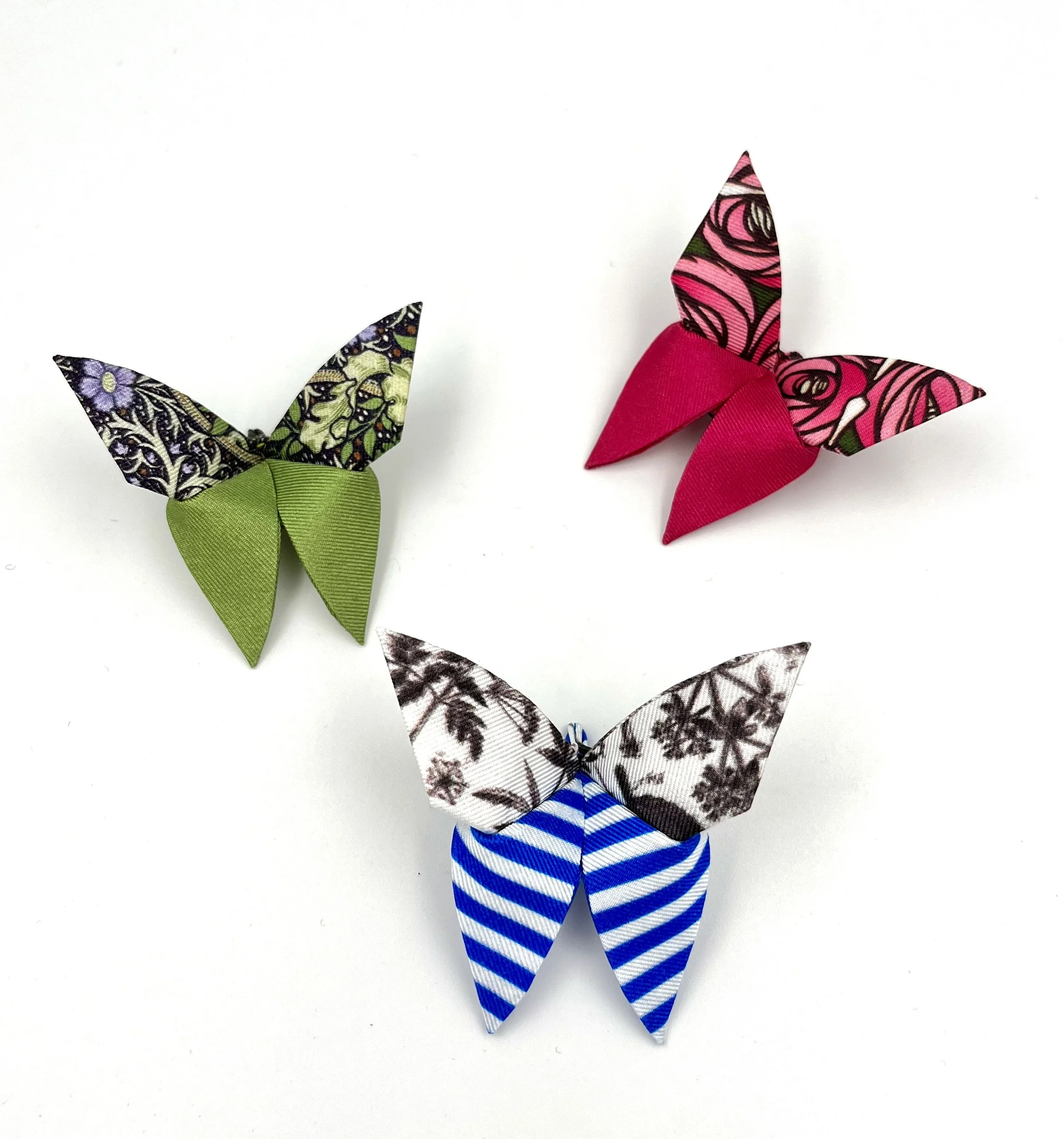 Origamis en forme de papillons réalisés avec des feuilles en tissu à motifs colorés, certains avec des rubans attachés à la base.