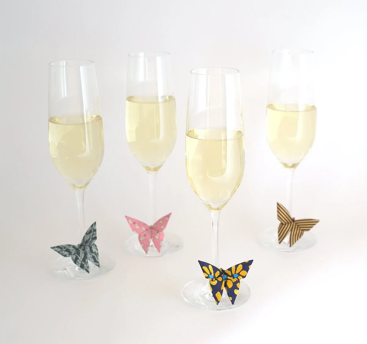 Trois flûtes de champagne avec des papillons en papier décoratifs à la base, sur fond blanc.