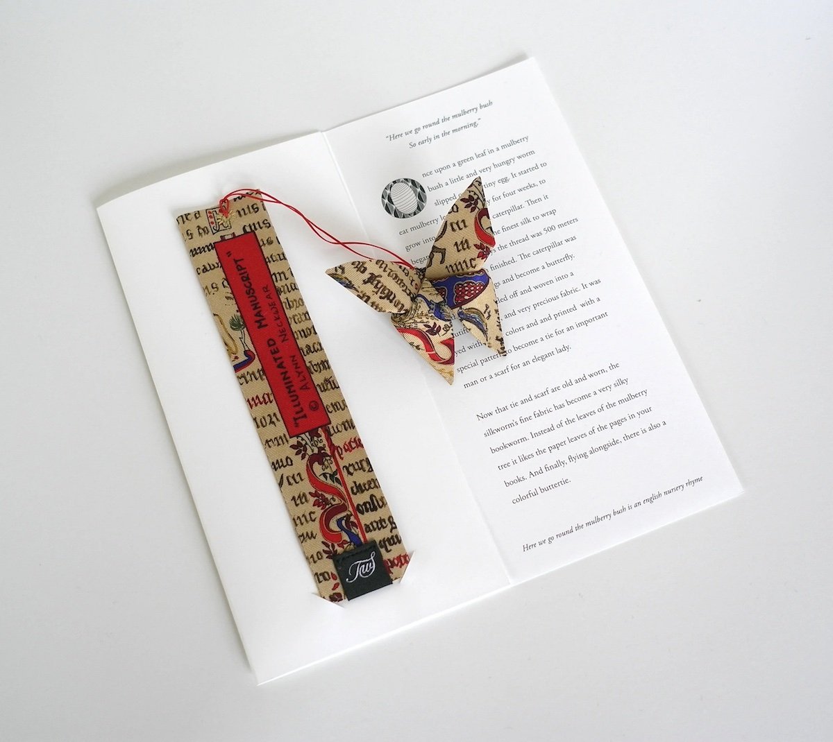 Un livre ouvert avec un marque-page en forme de foulard fait de tissu imprimé, un papillon en tissu assorti posé sur le livre, et du texte en anglais visible sur la page.