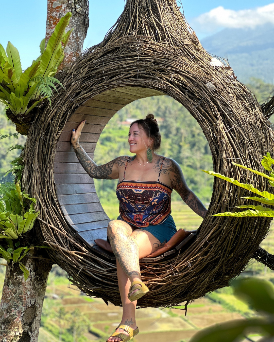 Woman sitting in a nest-like hanging chair in Indonesia in a lush outdoor setting, reflecting the creative, nature-inspired perspective behind Trillium Creative Studio