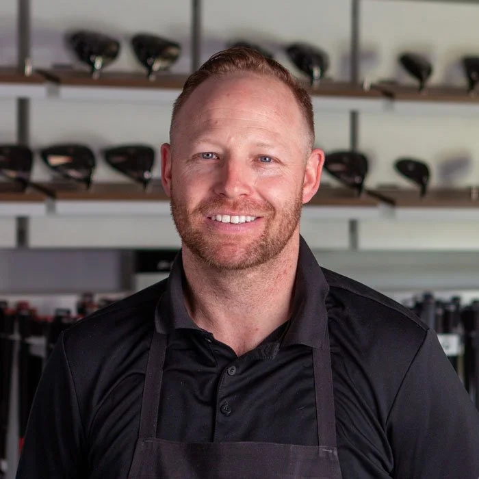 Fairview Mountain Golf Club Head Chef, Nick Atkins, standing in the fitting bay in front of shelves filled with golf clubs and golf bags.