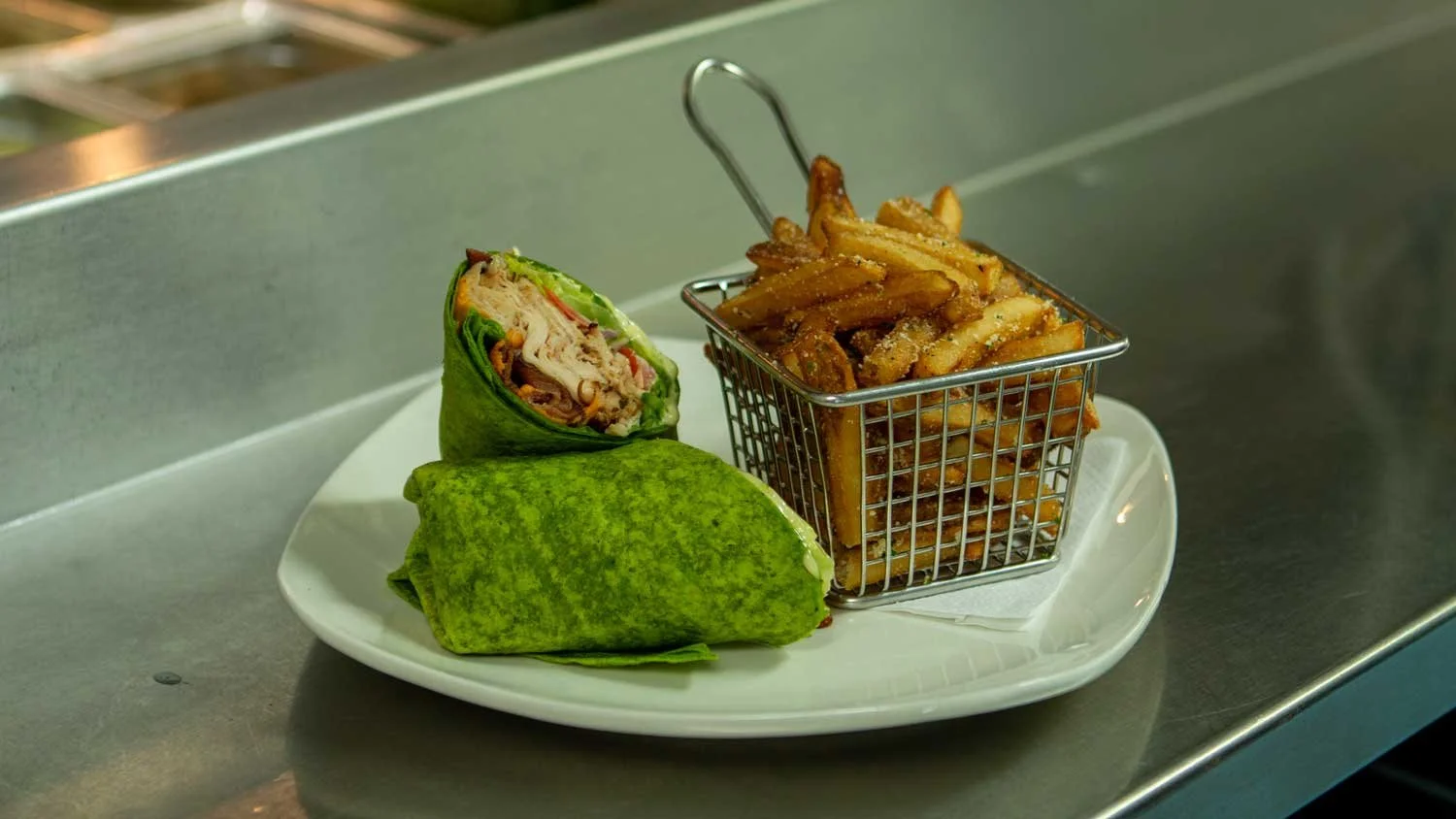 A plate with a chicken wrap and a side of French fries in a small metal basket