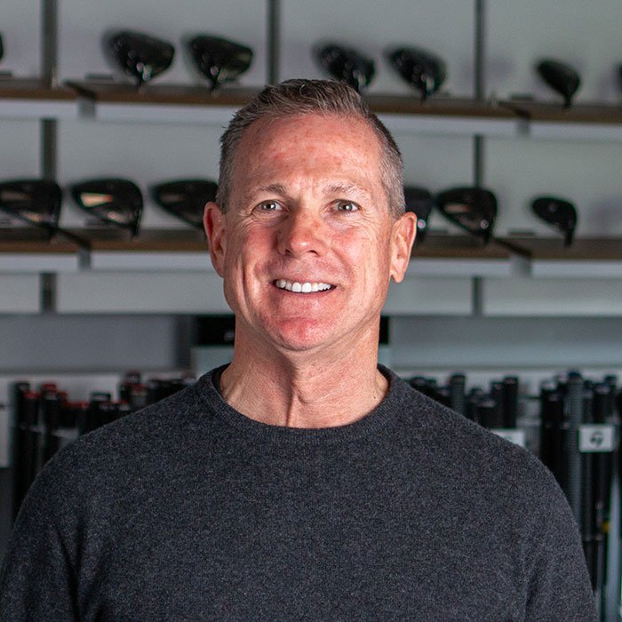 Fairview Mountain Golf Club COO, Brian McDonald, standing in the fitting bay in front of shelves filled with golf clubs and golf bags.