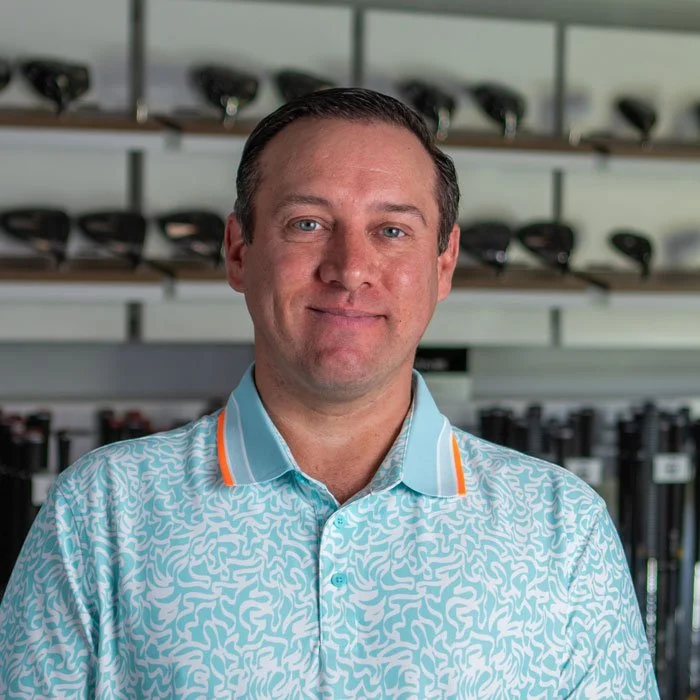 Fairview Mountain Golf Club Front of house manager, Jordan Shoemaker, standing in the fitting bay in front of shelves filled with golf clubs and golf bags.