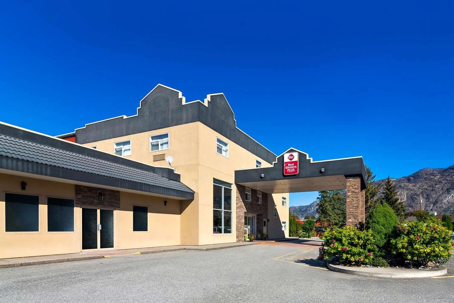 Exterior of a Best Western Plus hotel building with a blue sky background, surrounded by greenery and mountains.