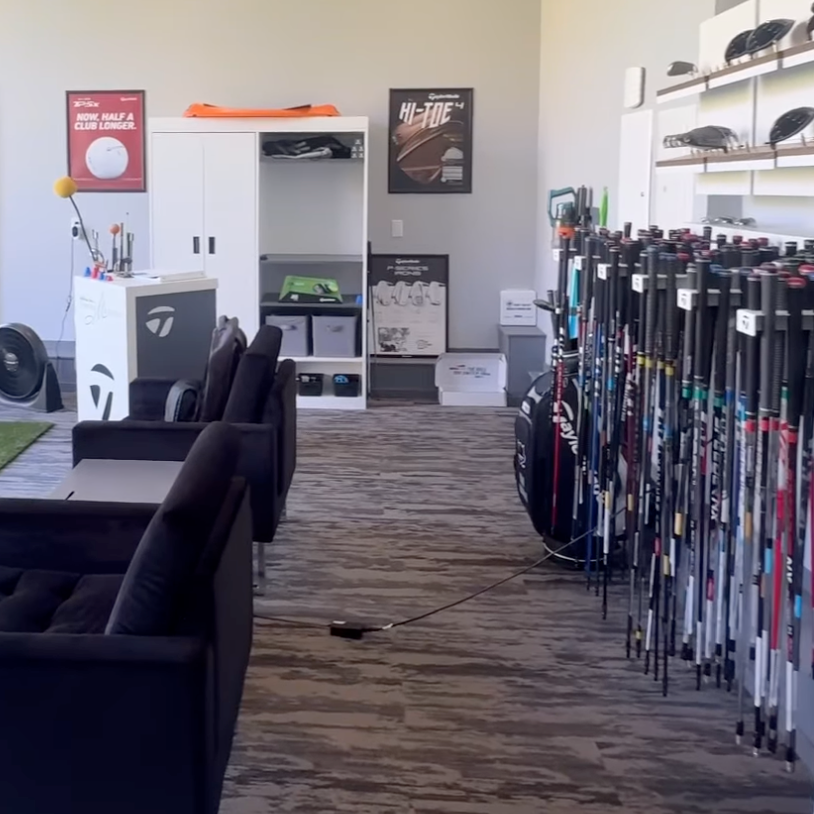 Fairview Mountain Golf Club fitting bay with clubs lined up on the right and seating area on the left, posters on the wall, and golf accessories and equipment displayed.