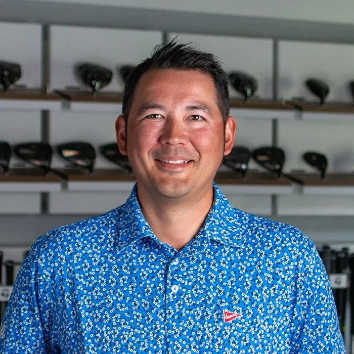 Fairview Mountain Golf Club superintendent, Daniel Lee, standing in the fitting bay in front of shelves filled with golf clubs and golf bags.