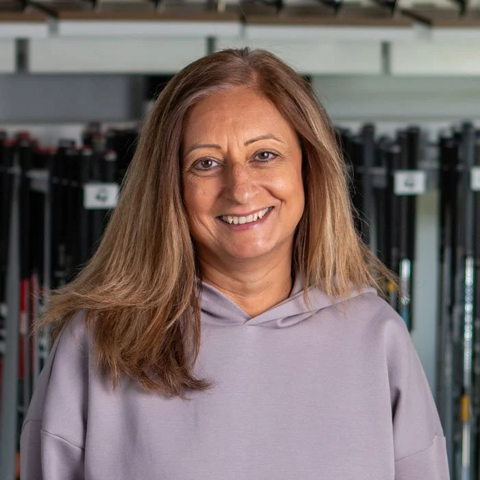 Fairview Mountain Golf Club accountant Shie Hyland, smiling, wearing a light gray hoodie, standing in front of shelves with golf clubs.