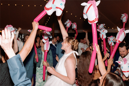 People celebrating at a party, holding pink inflatable horse toys above their heads in a festive setting.