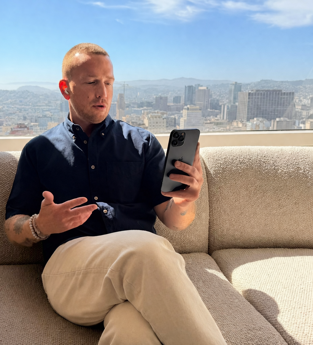Un homme assis sur un canapé regarde son téléphone portable dans un bâtiment avec une grande vue sur une ville.