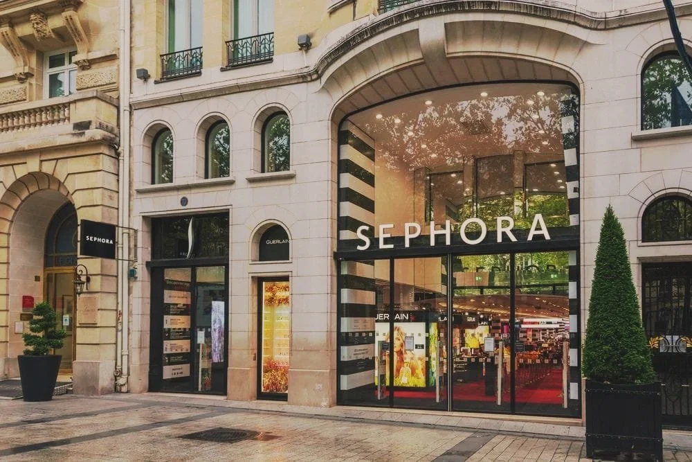 Vue d'un centre commercial Sephora avec une façade en verre et un grand panneau noir et blanc, entouré de bâtiments anciens.