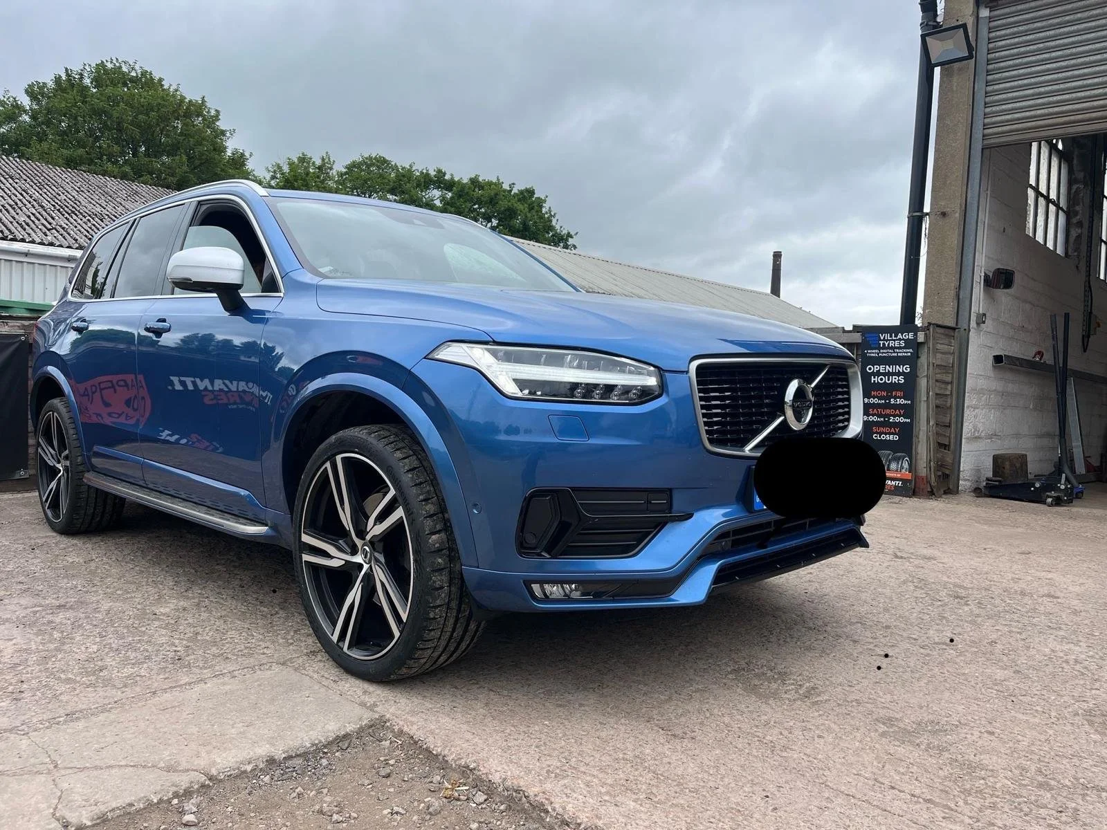 Blue Volvo SUV parked outside a vehicle repair shop on a cloudy day.