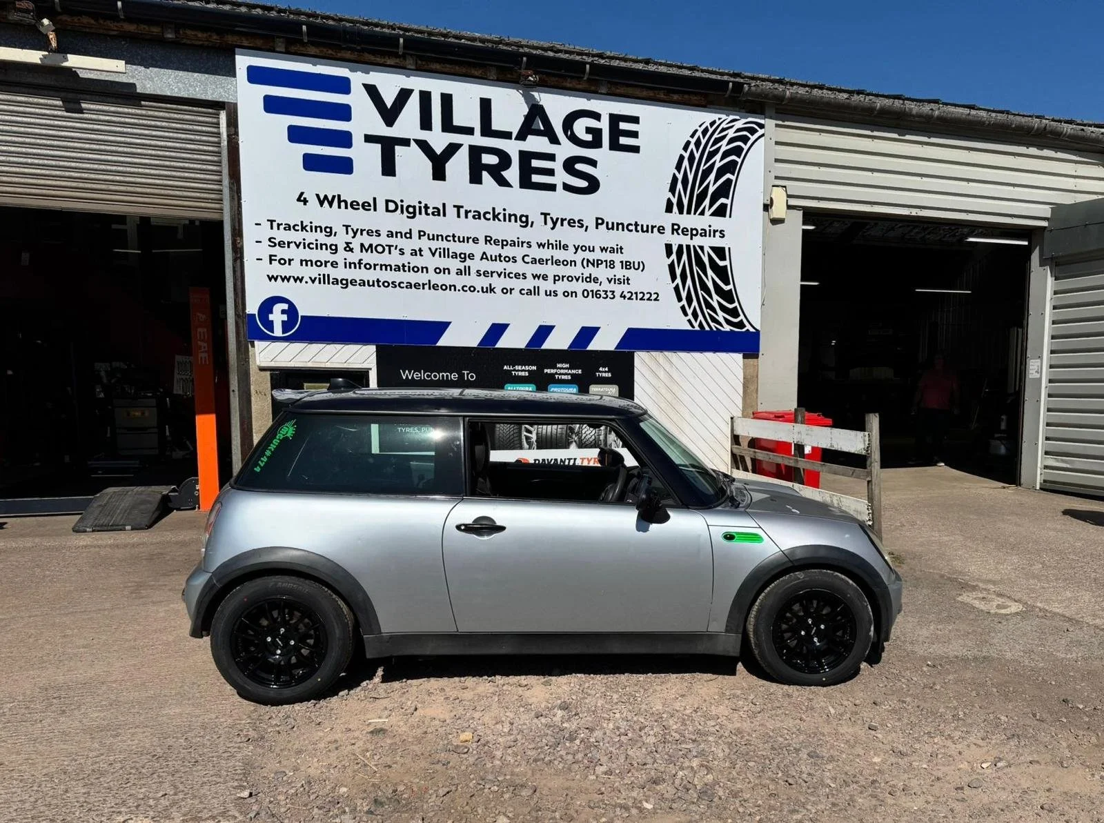 A silver compact car parked outside an auto repair shop with a large sign advertising tire services and repairs.