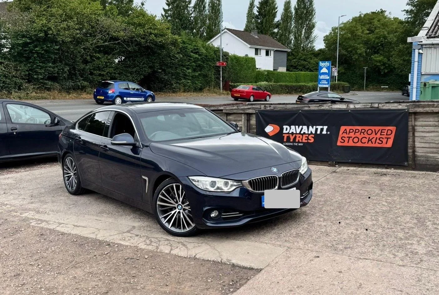 Black BMW parked in a lot with a sign for Davanti Tyres, approved stockist, in the background, other cars on the street and trees.